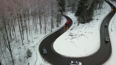 Cars-and-bus-driving-up-the-mountains-on-curved-road-during-day-in-snowy-winter,-Black-Forest-Germany