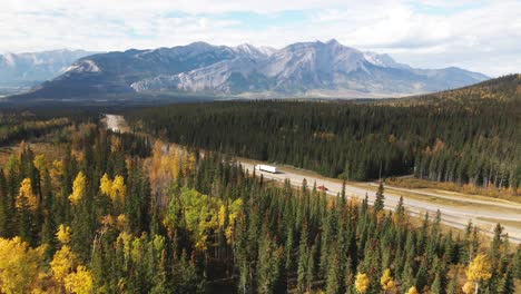 White-Semi-Truck-driving-on-the-Yellowhead-Highway-5-with-the-Jasper-National-Park-in-the-Background-in-the-fall-with-vivid-Color-Trees-on-a-cloudy-day