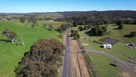 Road-through-Green-farmland-aerial-with-car-driving-through,-Australia