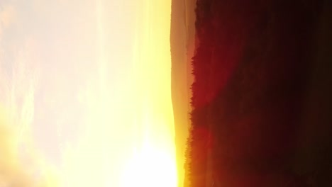 Vertical-drone-shot-intense-fiery-sunset-in-nature-over-forests-and-fields