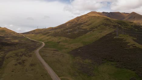 Aerial-descend-towards-a-dirt-road-leading-through-golden-brown-mountains