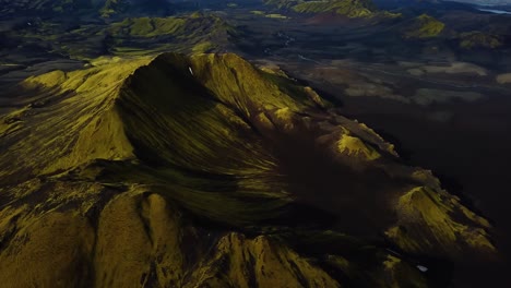 Aerial-landscape-view-of-Icelandic-highlands,-with-dark-hills-and-mountains,-covered-in-bright-green-grass,-on-a-cloudy-day