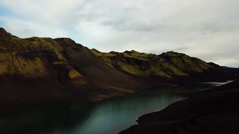 Aerial-landscape-view-of-a-turquoise-volcanic-lake-in-the-Icelandic-highlands-mountains,-on-a-cloudy-day