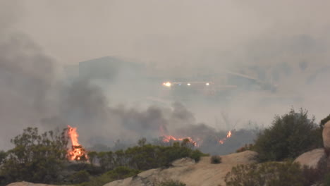 Los-Arbustos-En-Llamas-Durante-El-Incendio-De-Fairview-En-Hemet-California,-Con-Las-Luces-Intermitentes-De-Los-Servicios-De-Emergencia-Visibles-A-Través-Del-Humo-Feroz-En-El-Fondo