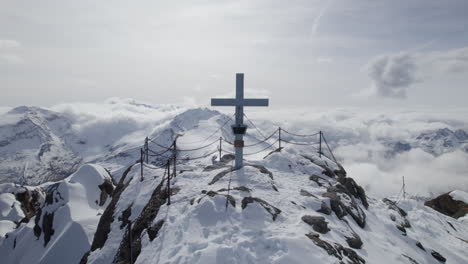 Close-up-drone-shot-of-summit-cross-on-snowy-mountain-peak-of-Kitzsteinhorn-during-sunny-day-in-Austria