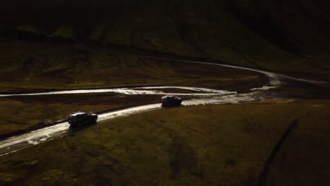 Aerial-landscape-view-over-four-wheel-drive-cars-traveling-on-a-dirt-road-and-crossing-a-muddy-river,-in-the-icelandic-highlands