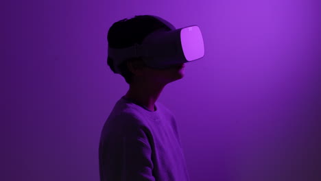 Teenager-wearing-futuristic-virtual-reality-headset-reaching-out-in-purple-lit-room