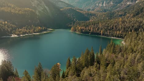 Drone-view-on-dolomites-small-lake-and-pine-forest-in-winter-season,-rocky-mountains-in-the-Italian-Alps,-in-golden-hour-at-sunrise