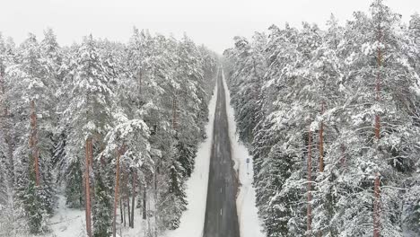 Snow-covered-forest-and-endless-country-road,-aerial-drone-view