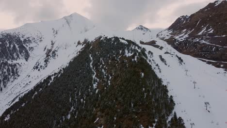 Un-Dron-Rodea-Los-árboles-Al-Lado-De-Una-Montaña-Con-Una-Pista-De-Esquí-En-Un-Aburrido-Día-De-Invierno