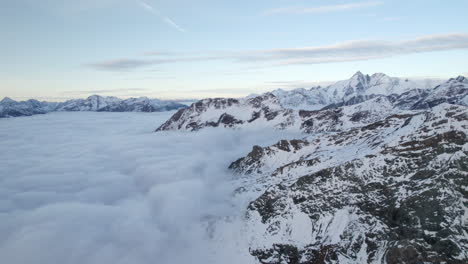 Drone-flying-over-low-clouds-covering-the-snowy-alpine-mountains-of-Grossglockner,-Austria