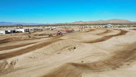 Motorcycle-takes-a-long-jump-off-a-dirt-ramp-on-an-off-road-racecourse---aerial-view