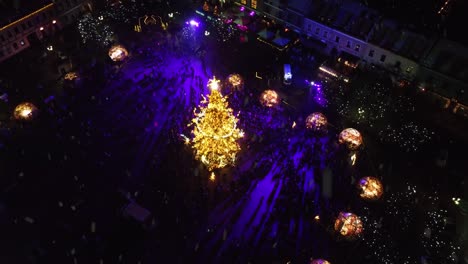 Vibrant-Christmas-tree-of-Kaunas-city-during-snowfall,-aerial-drone-orbit-view