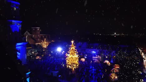 Glowing-Kaunas-City-Hall-and-Christmas-tree-during-snowfall,-aerial-view