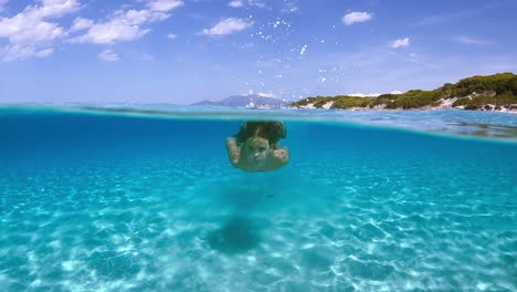 Amazing-scene-of-young-little-girl-swimming-beneath-sea-water-surface-of-Saleccia-beautiful-beach-in-Corsica-island,-France