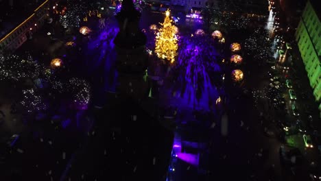 Orbiting-silhouette-of-Kaunas-city-hall-tower-with-view-of-glowing-Christmas-tree,-snowfall