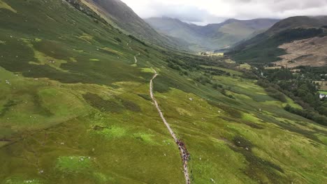4K-aerial-pan-of-hill-walkers-in-valley-starting-climb-to-Ben-Nevis,-drone-shot-above-Glen-Nevis,-Fort-William