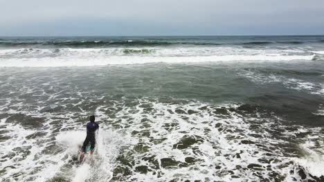 Kamerafahrt-Eines-Surfers,-Der-Ins-Meer-Läuft-Und-Sein-Surfbrett-Am-Sandstrand-Hält