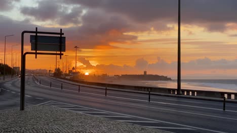 Weite-Sicht-Auf-Einige-Autos,-Die-Sich-In-Richtung-Eines-Wunderschönen-Sonnenaufgangs-In-Der-Nähe-Des-Strandes-In-Carcavelos,-Portugal,-Bewegen