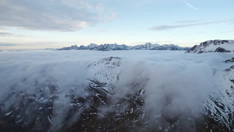 Aerial-panning-shot-revealing-a-curtain-of-clouds-falling-over-the-snow-capped-mountains-of-the-European-alps
