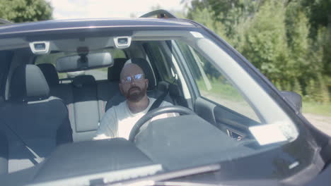 A-bearded-man-with-glasses-drives-on-a-rural-road,-turns-left-and-pulls-over