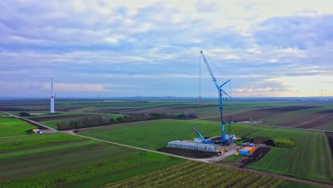 Construction-Of-Wind-Turbine-Tower-In-Green-Field---aerial-drone-shot