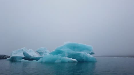 Panning-shot-of-bright-blue-Iceberg-floating-in-Jokusarlon-Glacier-Lagoon,-South-Iceland-ring-road-highlights
