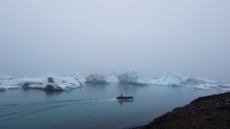 Person-in-bright-orange-jacket-on-zodiac-boat-approaching-big-icebergs-floating-in-Jokusarlon-Glacier-Lagoon