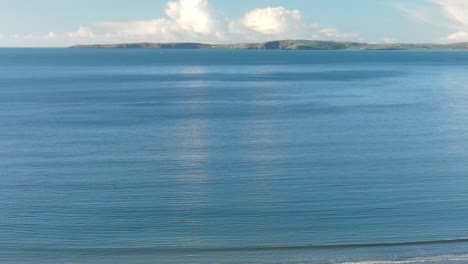Calm-winter-ocean-and-distant-Irish-coast-with-white-clouds-on-a-clear-morning-sky