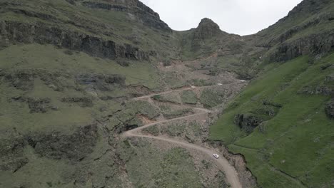 Retreating-aerial-of-Sani-Pass-gravel-switchbacks,-vehicles-driving-up