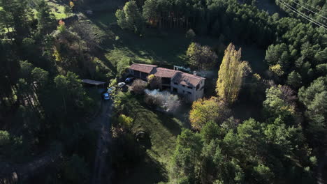 Aerial-view-over-Saldes-rural-village-farmhouse-surrounded-by-lush-green-Pedraforca-woodland,-Catalonia