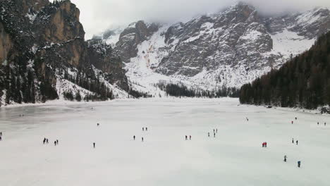 Touristen,-Die-Auf-Dem-Zugefrorenen-Pragser-See-Mit-Schneebedeckten-Dolomitbergen-Im-Hintergrund-Im-Trentino,-Italien,-Spazieren-Gehen