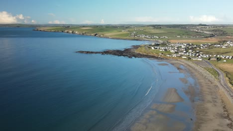 Winter-calm-blue-ocean-and-coastal-sandy-beach-with-small-village-in-the-distance,-Ireland,-aerial