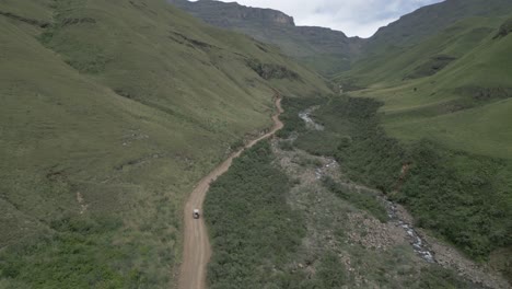 Dramatic-aerial-vista-as-SUV-drives-up-Sani-Pass-valley,-South-Africa