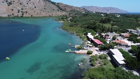 Hermoso-Lago-Kournas-En-Creta-Con-Botes-En-El-Agua-Turquesa-Que-Revela-Las-Montañas-Y-El-Cielo-Azul