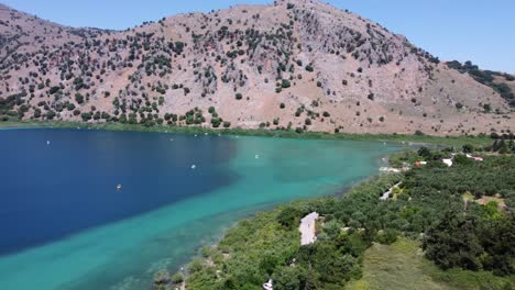 Hermoso-Lago-Kournas-En-Creta-Con-Botes-En-El-Agua-Turquesa,-Montañas-En-El-Paralaje-De-Fondo