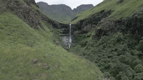 Aerial-flight:-Deep-rocky-valley-to-small-waterfall-off-green-plateau