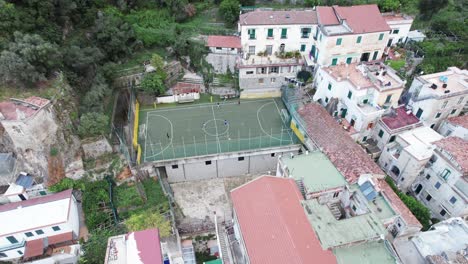 An-aerial-shot-circling-a-rooftop-soccer-or-football-pitch-as-kids-train-in-the-cliffs-of-Amalfi-town,-one-of-the-most-popular-tourist-destinations-on-the-famous-Amalfi-Coast-in-Italy