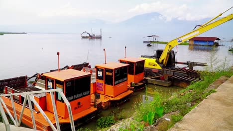 Heavy-dredging-equipment-backhoe-and-boats-docked-on-lake-shore-in-Indonesia