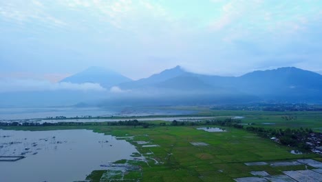 Drone-shot-of-rice-field-and-lake-with-mountain-range-on-background