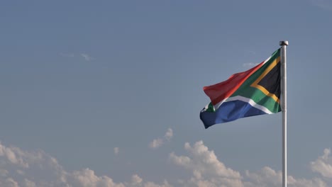 Flag-of-South-Africa-on-right-of-frame,-flutters-against-sunny-sky