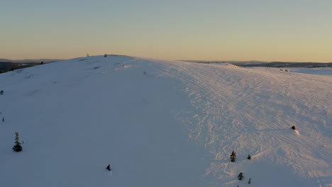 Snowmobiles-speed-up-snowy-Lapland-hillside-aerial-view-rising-to-Swedish-frozen-landscape-at-sunrise