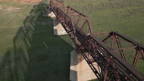 Person-walks-across-rusty-old-decommissioned-railway-bridge,-aerial