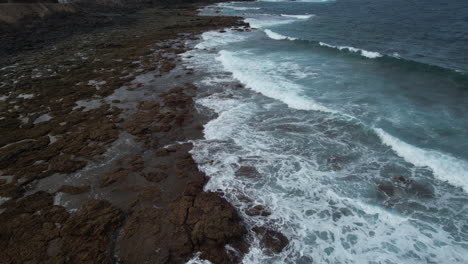 Filmische-Luftaufnahme-über-Dem-Ufer-Mit-Felsen-Des-Strandes-Von-Punta-De-Galdar-Auf-Der-Insel-Gran-Canaria-Und-Enthüllt-Die-Häuser-In-Der-Nähe-Der-Küste