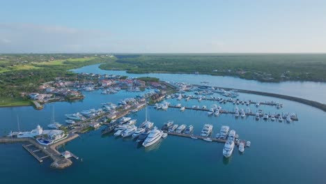 Aerial-backwards-shot-of-beautiful-Casa-de-Campo-Marina-with-luxury-yachts-in-La-Romana,-Dominican-Republic---Ascending-drone-shot