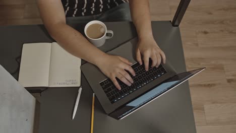 Top-Down-Aufnahme-Einer-Molligen-Person,-Die-An-Ihrem-Schreibtisch-Am-Laptop-Arbeitet,-Während-Sie-Einen-Kaffee-Trinkt,-Multi-Task-Konzept