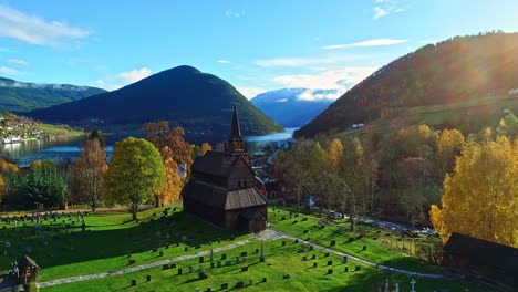 Aerial-backwards-shot-of-Norwegian-village-with-church-and-cemetery-during-Beautiful-autumn-day---Mountains-and-fjord-water-in-background