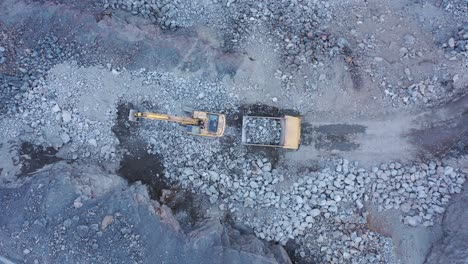 Aerial-panning-shot-of-excavator-placing-rocks-dump-truck