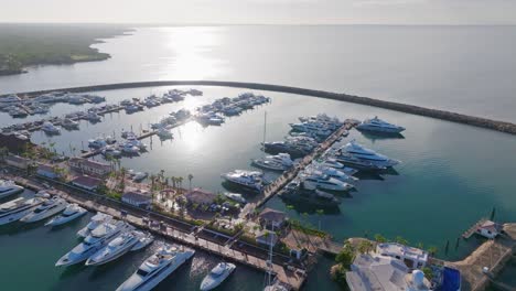 Aerial-orbiting-shot-of-beautiful-marina-with-luxury-yachts-during-sunset-time-with-water-reflection---La-Romana,-Dominican-Republic