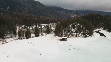 Lake-Braies-During-Winter-With-People-Walking-On-The-Ice-In-Trentino,-Italy---aerial-drone-shot